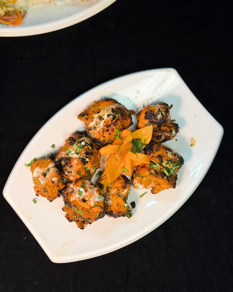 Achari tikka &mdash; pieces of chicken in a deep orange pickling-spice marinade, blistered from the tandoor