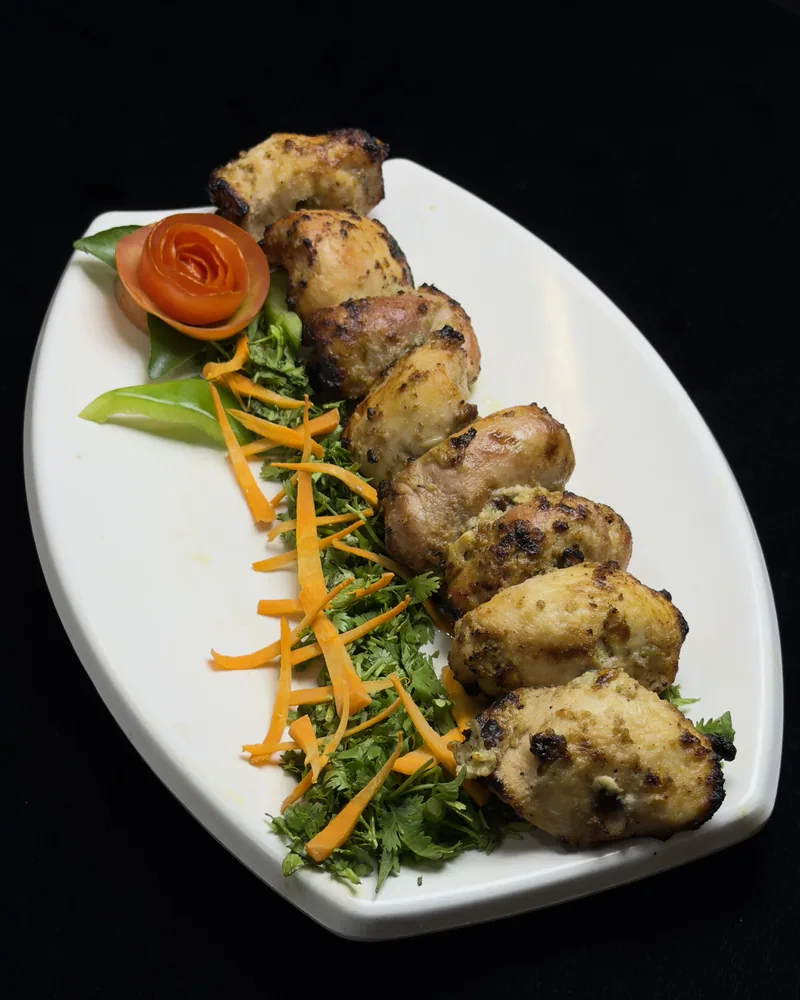 Malai tikka &mdash; pale, cream-marinated chicken pieces lined up on a long plate with carrot and coriander