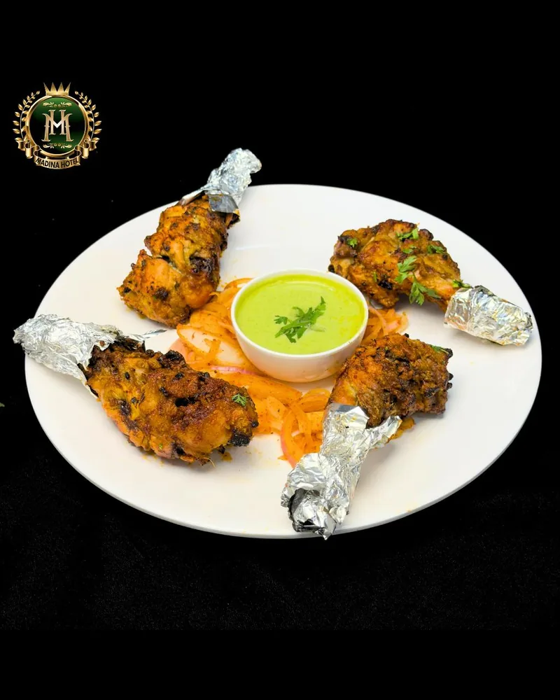 A plate of tangdi kebab at Madina Hotel &mdash; four chicken drumsticks with foil-wrapped bones arranged around a bowl of green chutney