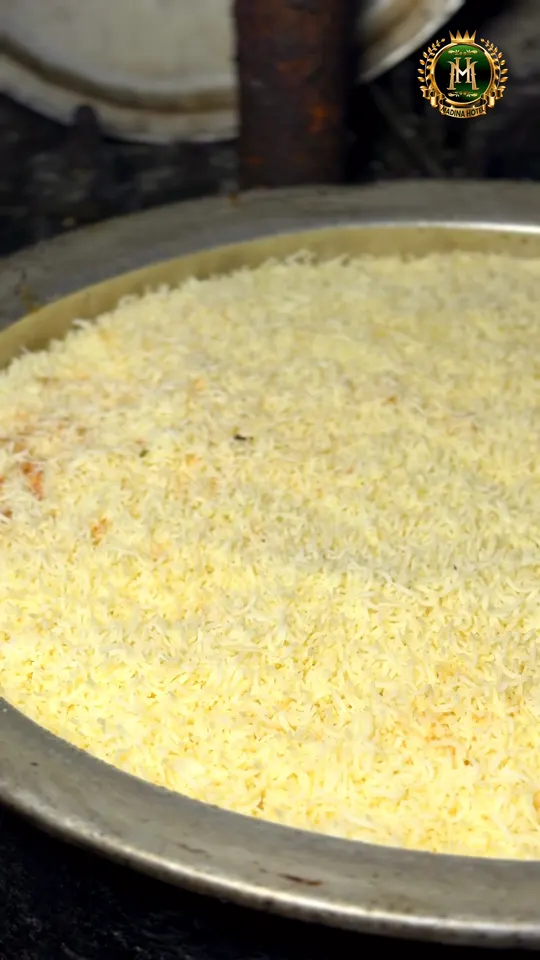 Long-grain rice spread in an even layer over marinated meat in a wide cooking degh, ready for the dum