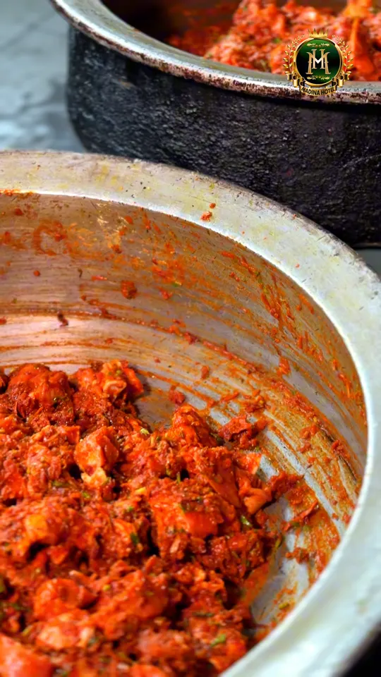 A large aluminium pot of deep red marinated meat being turned through by hand in the Madina Hotel kitchen