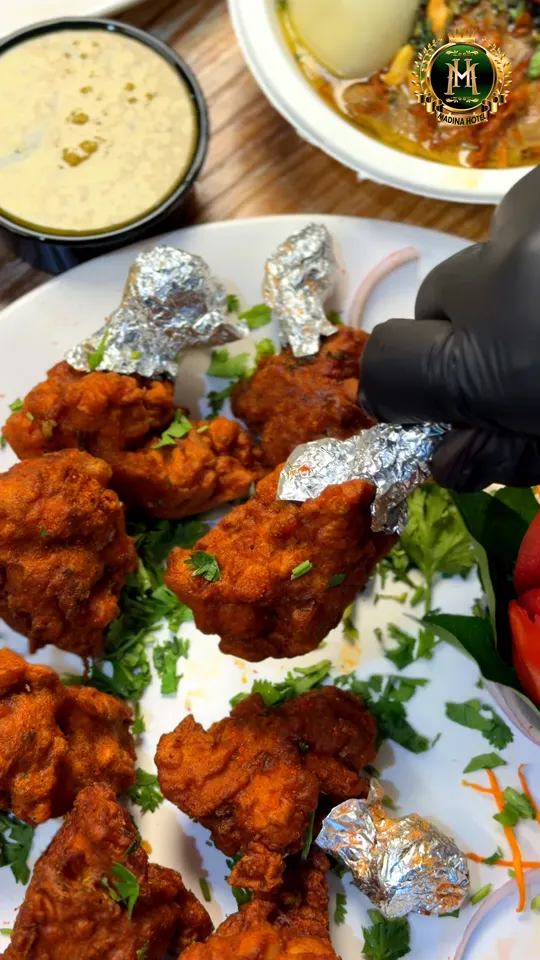 A platter of kebabs and fried chicken pieces garnished with coriander, plated at Madina Hotel